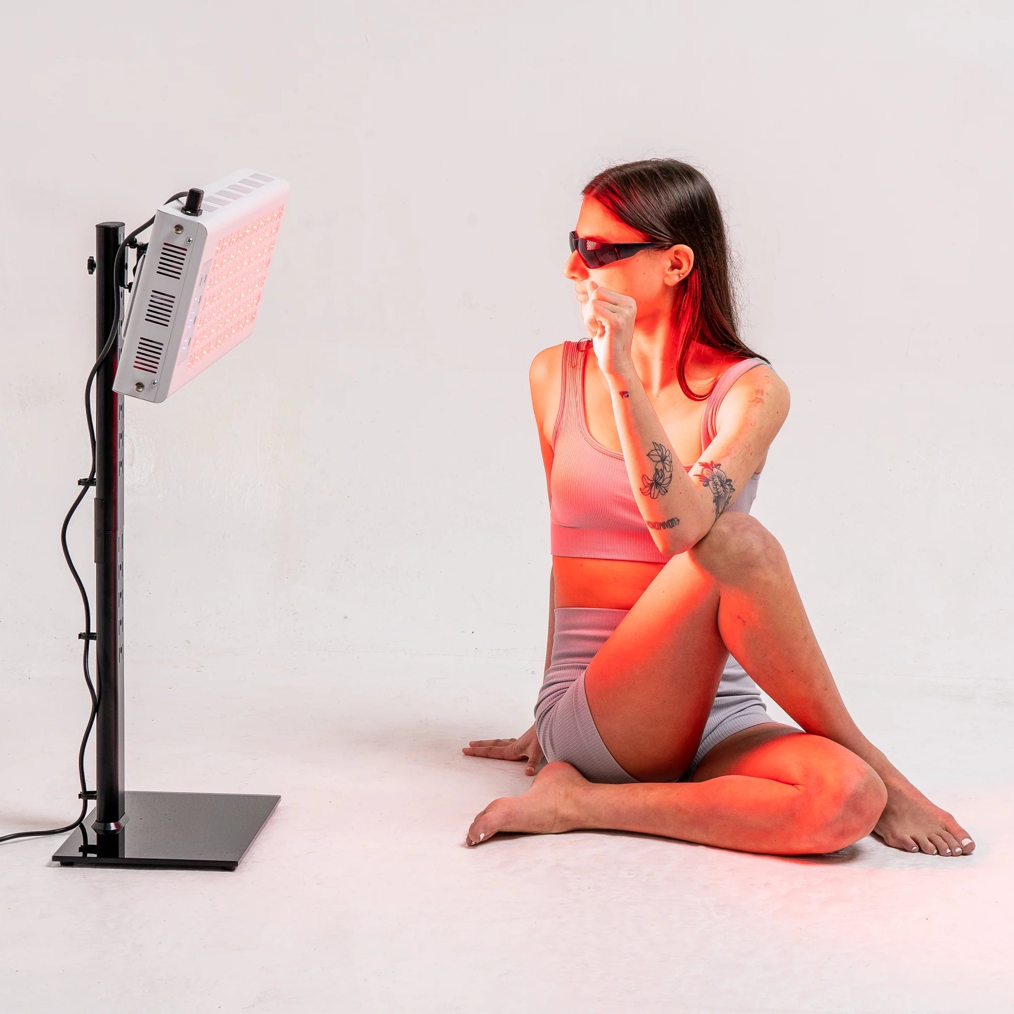 Person seated near the RedRush 400 PULSE targeted red and near-infrared light panel while wearing protective glasses