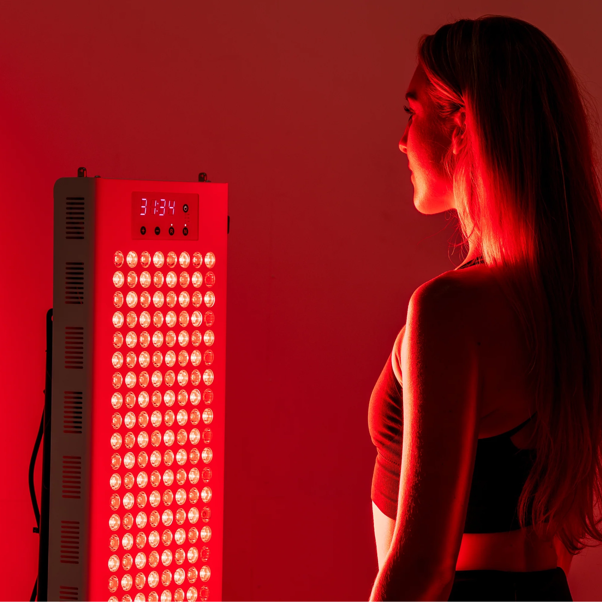 Person standing in front of the illuminated RedRush 840 PULSE full-body red and near-infrared light panel
