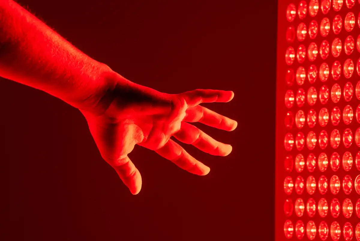 Hand outstretched toward a glowing RedRush PULSE red light therapy panel