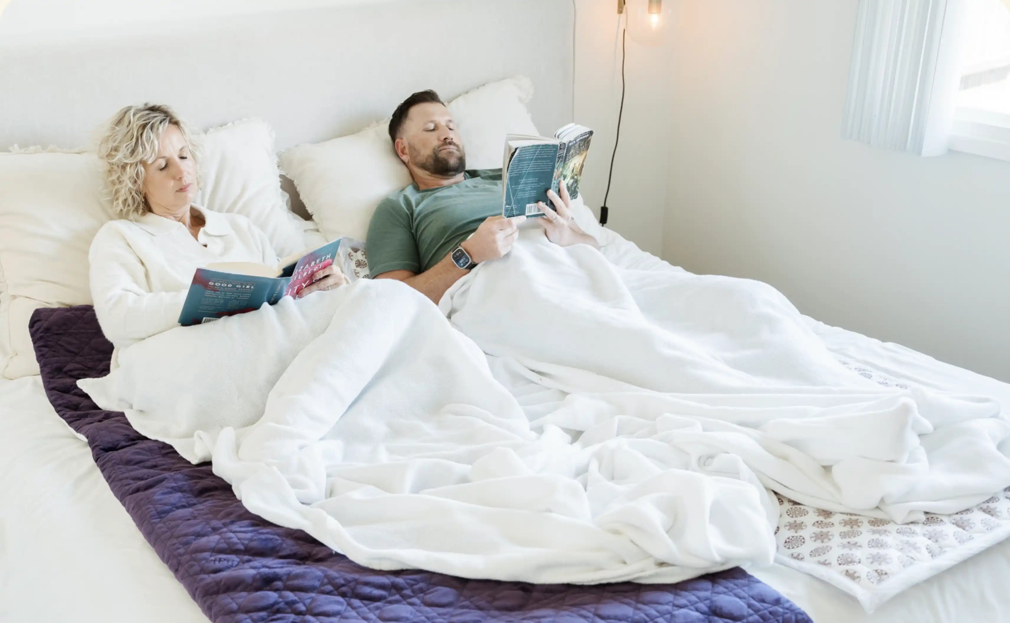 Two people lying in bed reading books on top of BioMat infrared mats.
