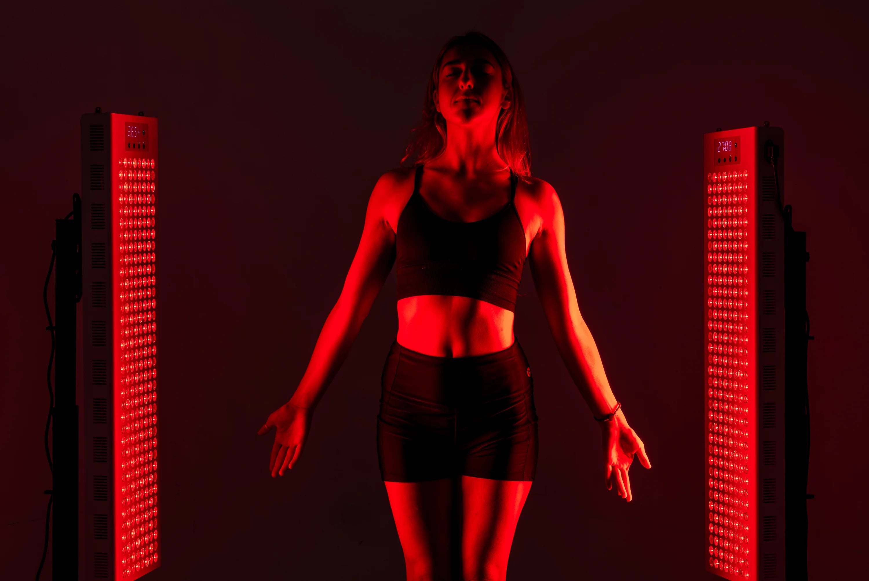 Person in black athletic wear standing between two red LED panels on a dark background