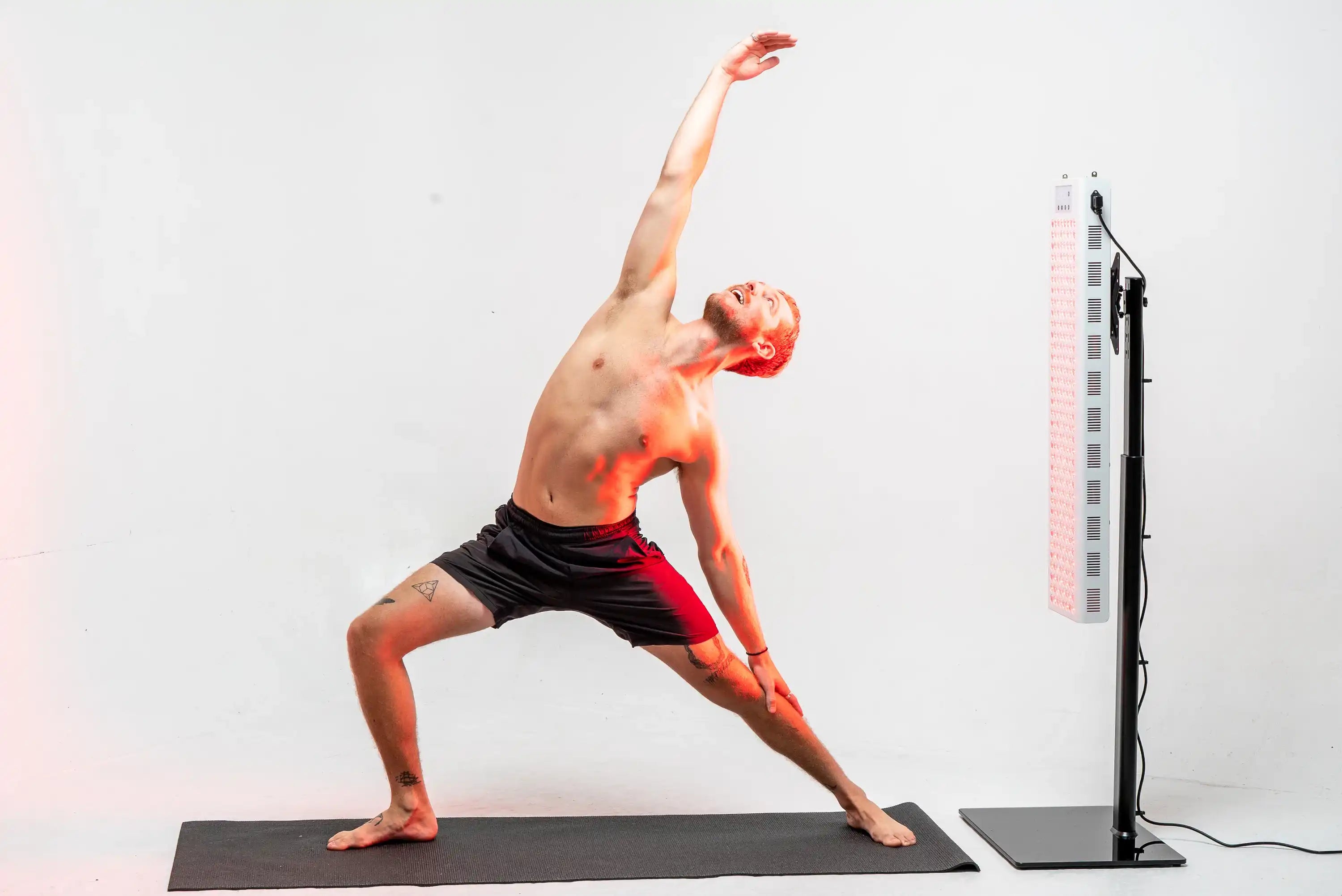 Person doing reverse warrior pose beside the illuminated RedRush 840 PULSE full-body red and near-infrared light panel
