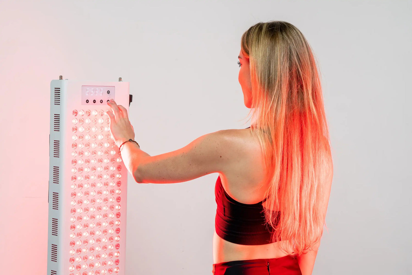 Person adjusting the controls on the RedRush 840 PULSE full-body red and near-infrared light panel