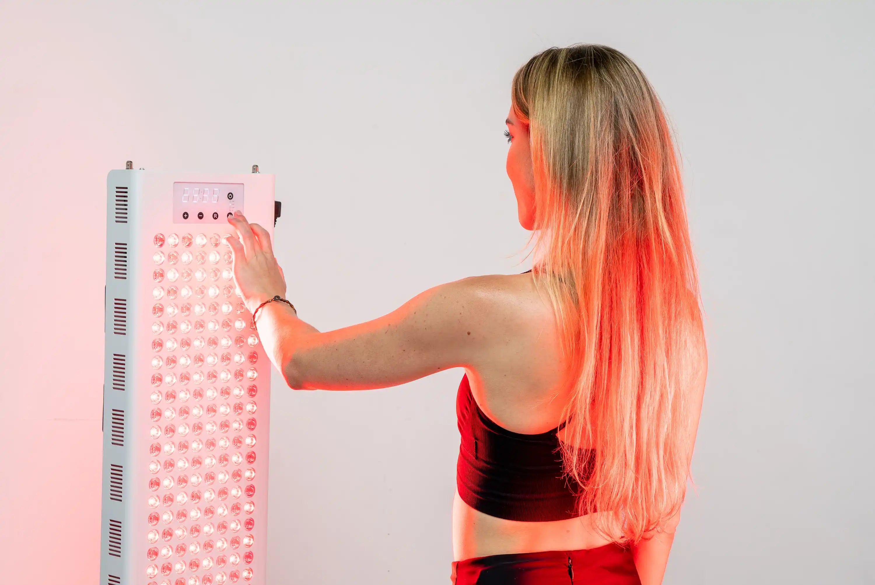 Person adjusting the controls on the RedRush 840 PULSE full-body red and near-infrared light panel
